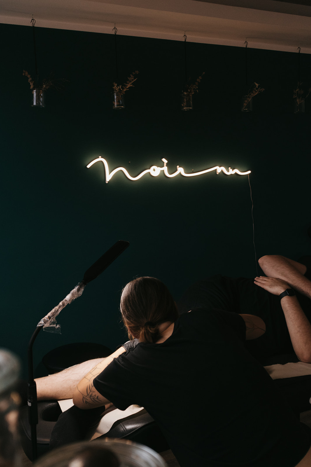 Tätowierung im Noir nu Studio unter einem leuchtenden Neon-Schriftzug.